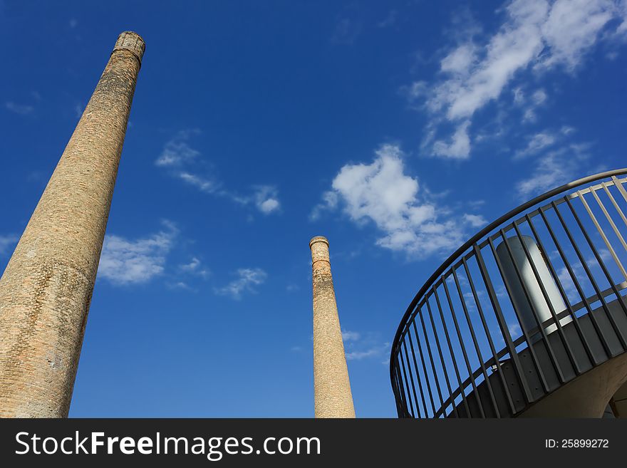 Two disused old chimneys against a blue sky and a portion of a more recent building. Two disused old chimneys against a blue sky and a portion of a more recent building