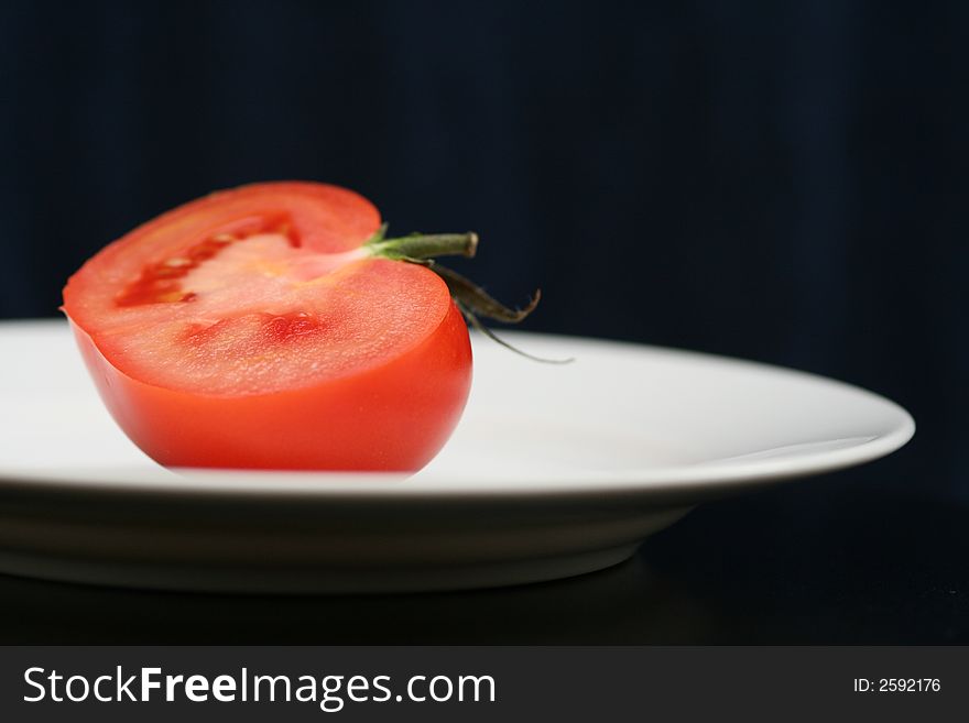 Tomato with stem on the plate and black background