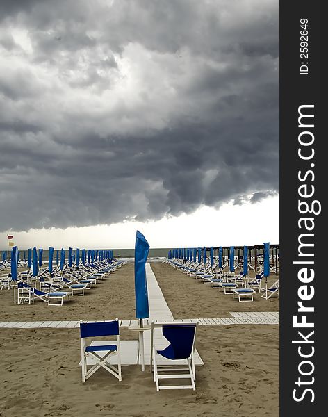 Menacing clouds over a beach with umbrella and seats, Italy. Menacing clouds over a beach with umbrella and seats, Italy