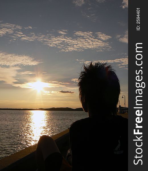 A man sitting along a jetty, looking out towards the open sea and the setting sun. A man sitting along a jetty, looking out towards the open sea and the setting sun.