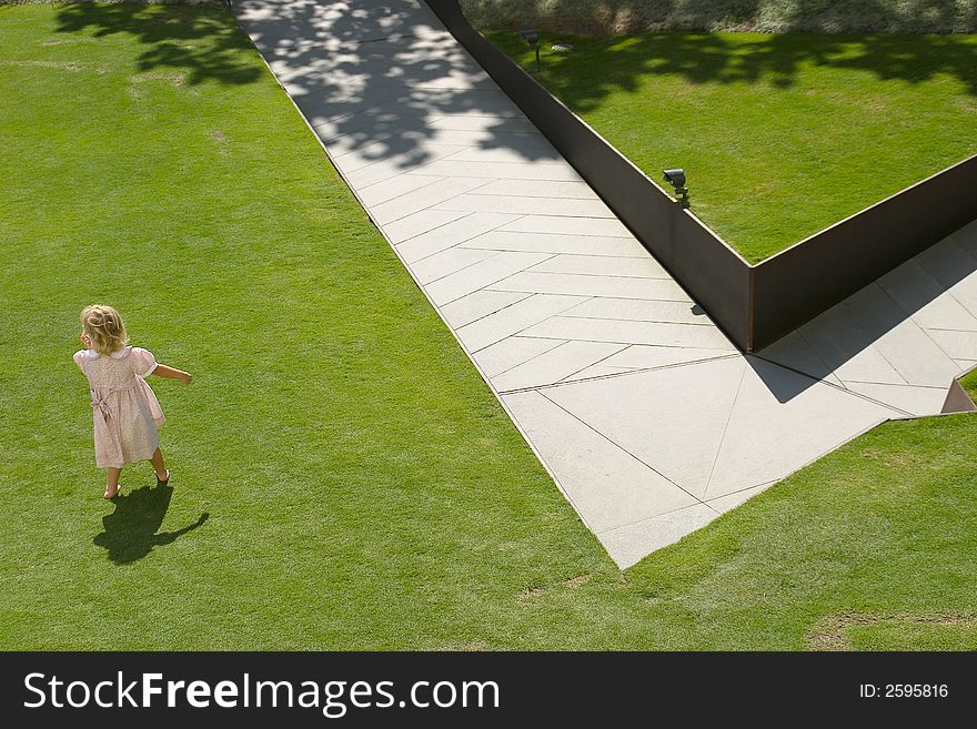 Girl child playing in park with green grass and diagonal sidewalk. Girl child playing in park with green grass and diagonal sidewalk.