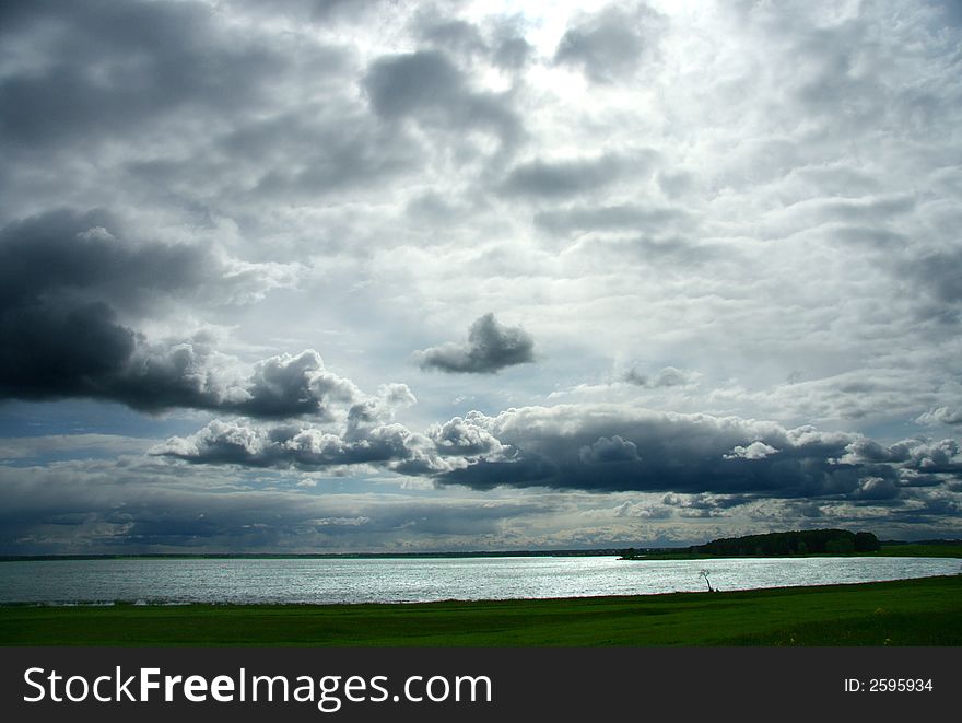 Landscape with the cloudy sky, lake, coast and a wood. Landscape with the cloudy sky, lake, coast and a wood.