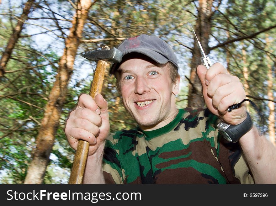 Man with with funny smile (may be little crazy) at nature. He is holding hammer and penknife. Man with with funny smile (may be little crazy) at nature. He is holding hammer and penknife.