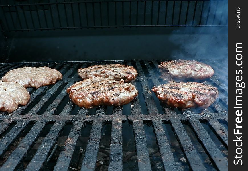 Photo of a burgers being cooked on a smoker grill. Photo of a burgers being cooked on a smoker grill