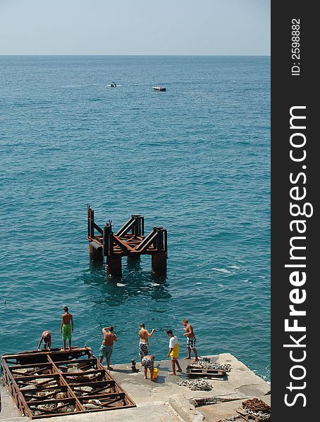 Some boys play and fish off a dock in the Mediterranean. Some boys play and fish off a dock in the Mediterranean.