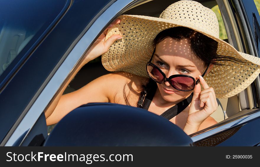 Beautiful female driver in a straw sun hat and sunglasses peering over her glasses checking her side mirror. Beautiful female driver in a straw sun hat and sunglasses peering over her glasses checking her side mirror