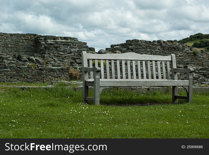 A sterdy bench on a green lawn, backed by an old crumbling castle wall. A sterdy bench on a green lawn, backed by an old crumbling castle wall.