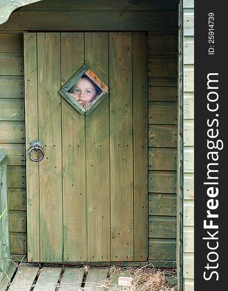 Child boy looking through the small window in a door whilst playing in a wooden garden shed. Child boy looking through the small window in a door whilst playing in a wooden garden shed.