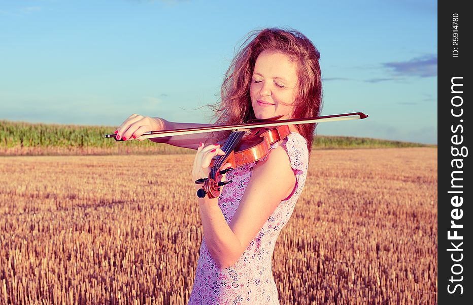 Redhead woman playing violin outdoors on the field in summer evening. Split toning.