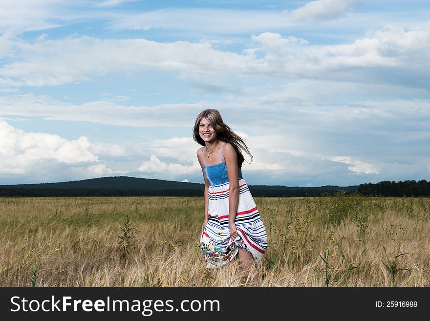 Fashion photo of young beautiful woman standing on a field of wheat against a background of sky and clouds