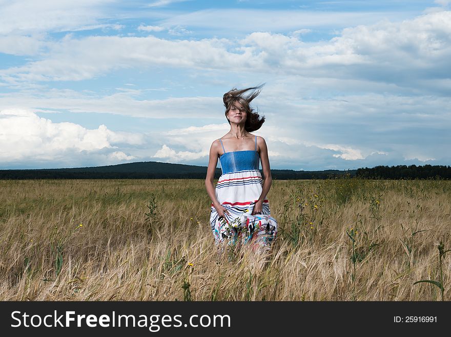 Fashion photo of young beautiful woman standing on a field of wheat against a background of sky and clouds