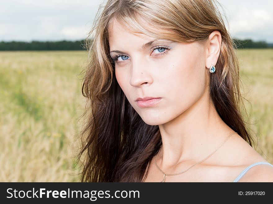 Fashion photo of young beautiful woman standing on a field of wheat against a background of sky and clouds