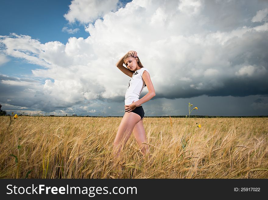 Fashion photo of young beautiful woman standing on a field of wheat against a background of sky and clouds