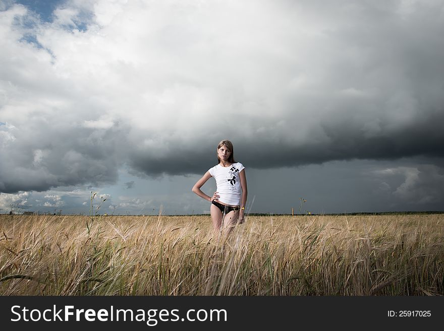 Fashion photo of young beautiful woman standing on a field of wheat against a background of sky and clouds