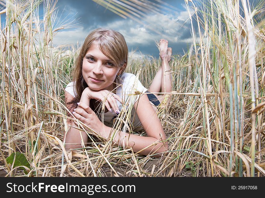 Fashion photo of young beautiful woman lies on a wheat field against a background of sky and clouds