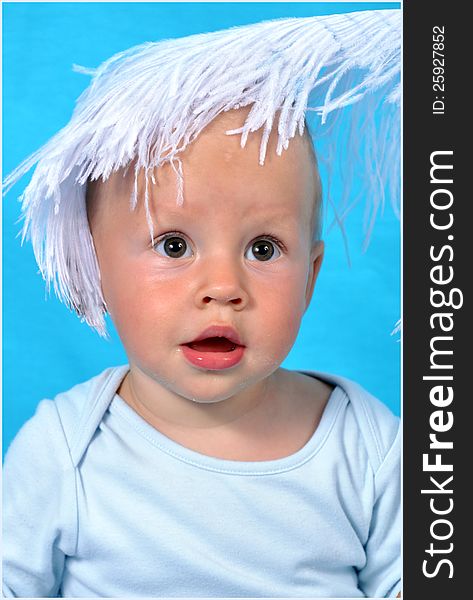 On a blue background a portrait of the child with a big fluffy white feather on the head. On a blue background a portrait of the child with a big fluffy white feather on the head