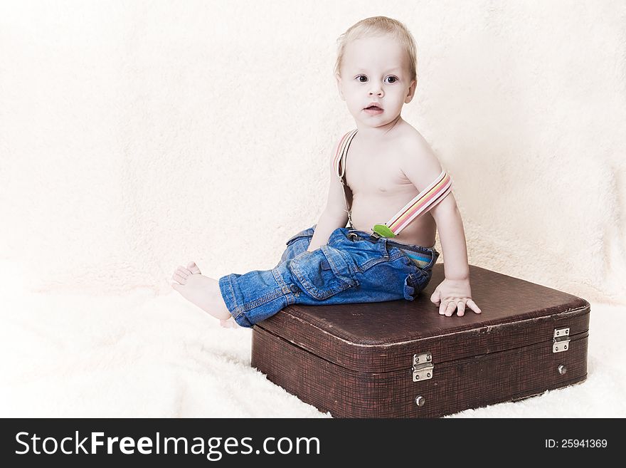 The child in jeans sits on an old suitcase. The child in jeans sits on an old suitcase