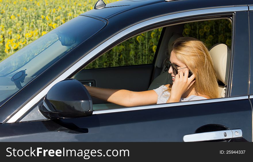 Woman driver talking on her mobile phone with her car safely pulled over to the side of the road near a field of sunflowers