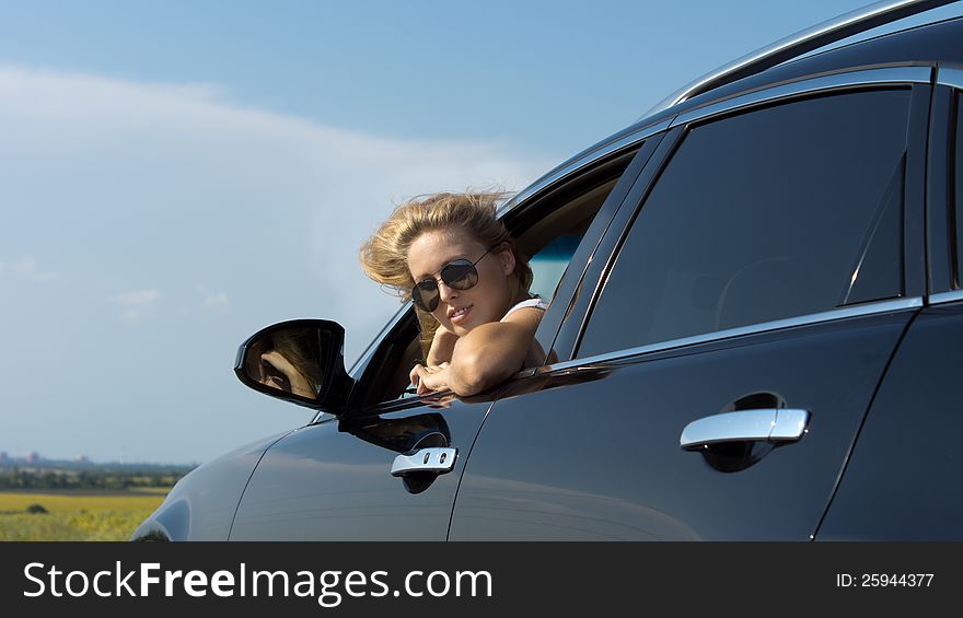 Low angle view of a blonde woman in sunglasses looking back out of a car window. Low angle view of a blonde woman in sunglasses looking back out of a car window