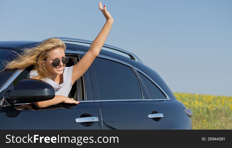 Beautiful blonde woman in sunglasses leaning out and waving from a car window. Beautiful blonde woman in sunglasses leaning out and waving from a car window