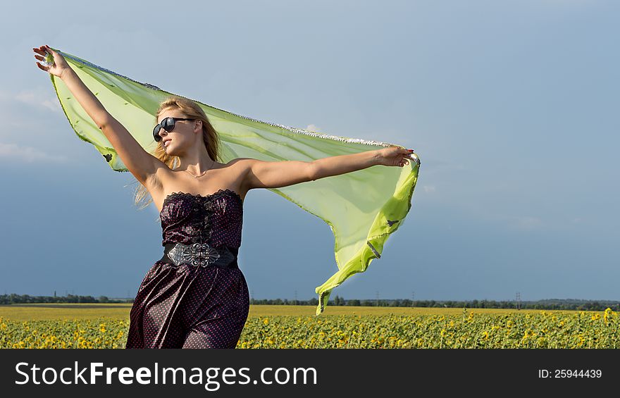 Beautiful blonde woman with a scarf held high in the air blowing in the wind standing in open countryside with a field of sunflowers. Beautiful blonde woman with a scarf held high in the air blowing in the wind standing in open countryside with a field of sunflowers