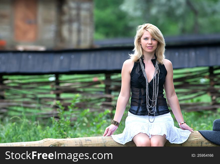 Girl is sitting on the background of the fence, it is made of twigs. Girl is sitting on the background of the fence, it is made of twigs