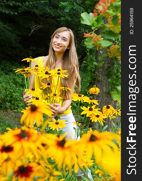 Close-up portrait of a young smiling  woman with yellow flowers against a background of trees. Close-up portrait of a young smiling  woman with yellow flowers against a background of trees