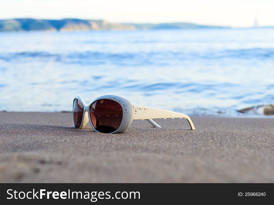 White sunglasses are in sand on shore of beach. White sunglasses are in sand on shore of beach