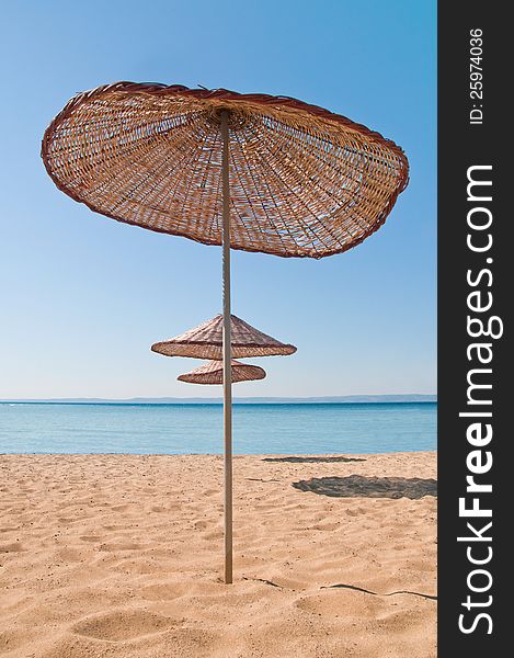 Vertical photo of a mat umbrella on a tropical beach. There are three umbrellas near the blue sea. There is noone in the photo. Vertical photo of a mat umbrella on a tropical beach. There are three umbrellas near the blue sea. There is noone in the photo.