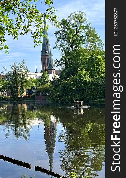 View on the church in Oldenburg from the castle garden. There is a large pond in front the buildings. Reflections of these buildings in the water