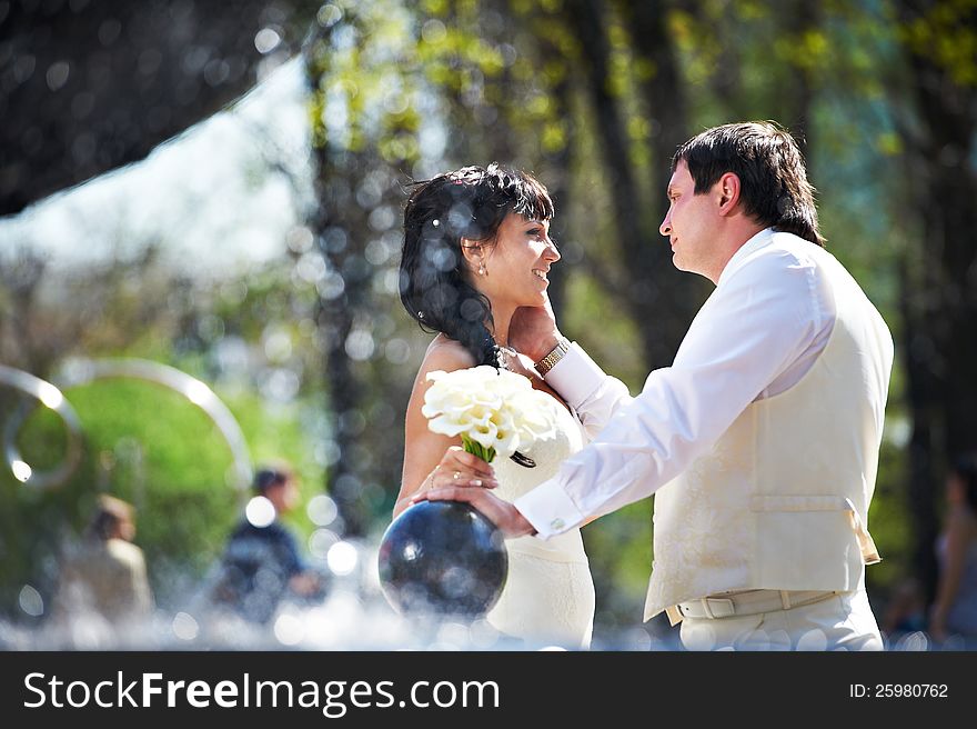 Happy bride and groom with bouquet near fountain