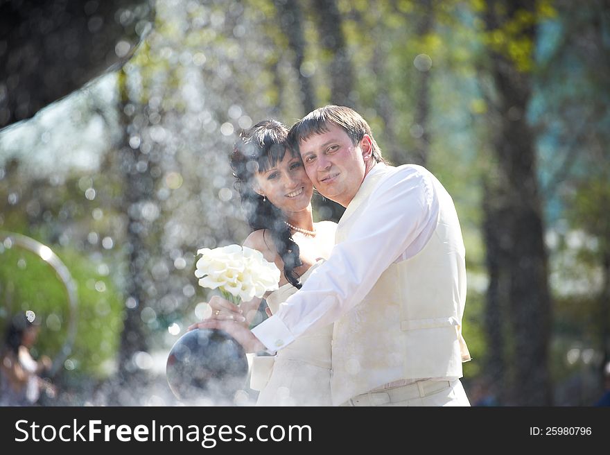Happy bride and groom with bouquet near fountain