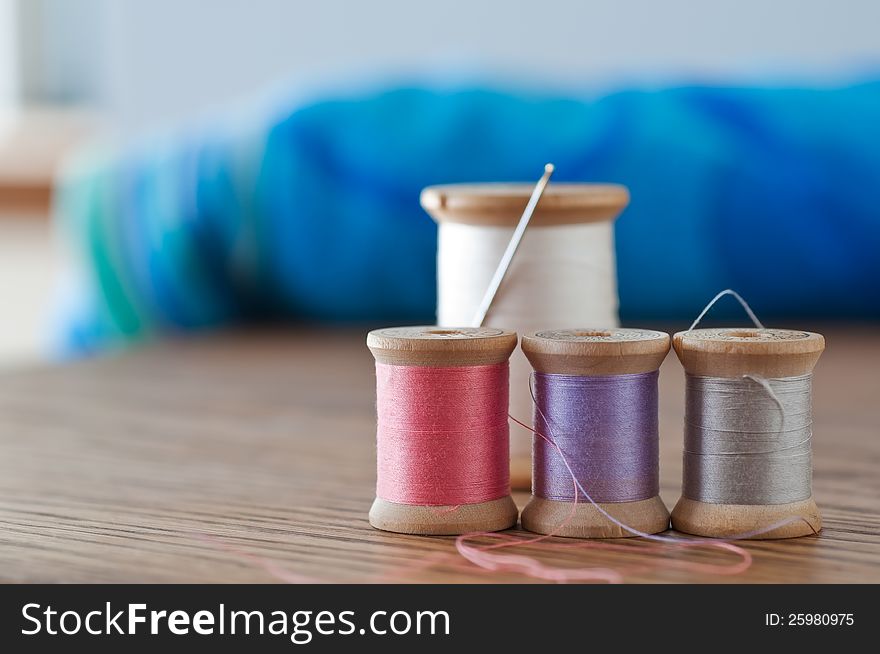 Four spools of thread plus needle in close focus with colorful background. Four spools of thread plus needle in close focus with colorful background