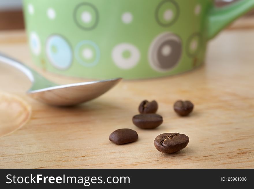 Close focus on coffee beans in front of cup and spoon. Close focus on coffee beans in front of cup and spoon