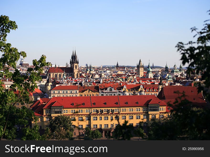 View of red roofs and high gothic towers between green leaves. Prague, Czech Republic. View of red roofs and high gothic towers between green leaves. Prague, Czech Republic