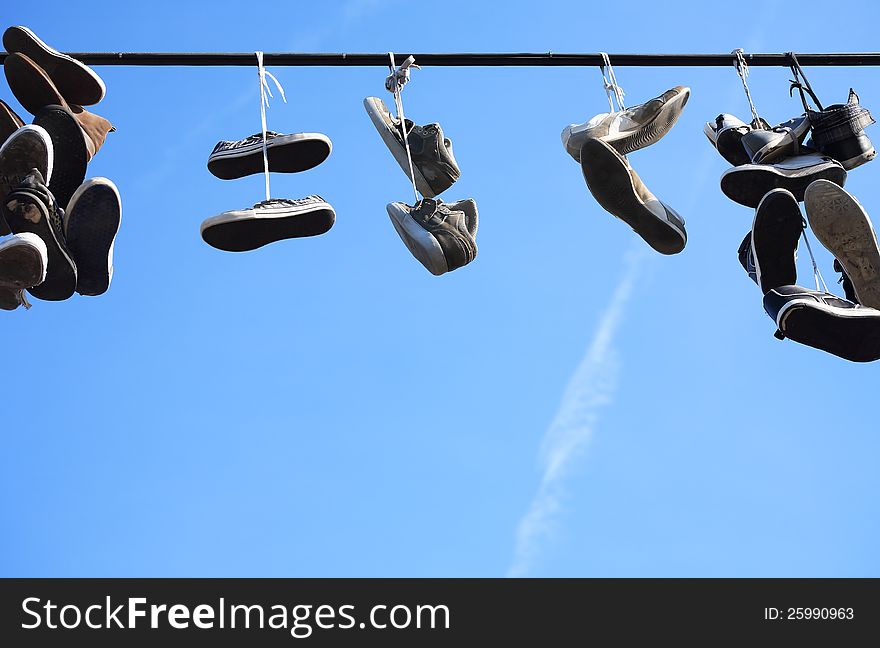 Lot of worn shoes hanging on wire against blue sky