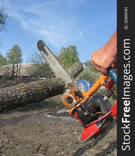 The man sawing the firewoods by petrol saw. The man sawing the firewoods by petrol saw