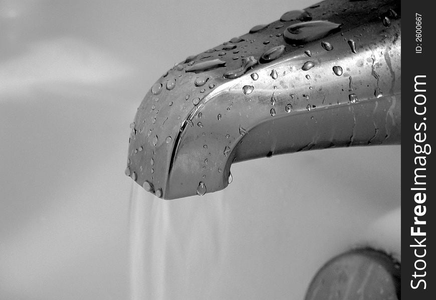 A running bathroom faucet coated in the water droplets of a dripping fixture. A running bathroom faucet coated in the water droplets of a dripping fixture.