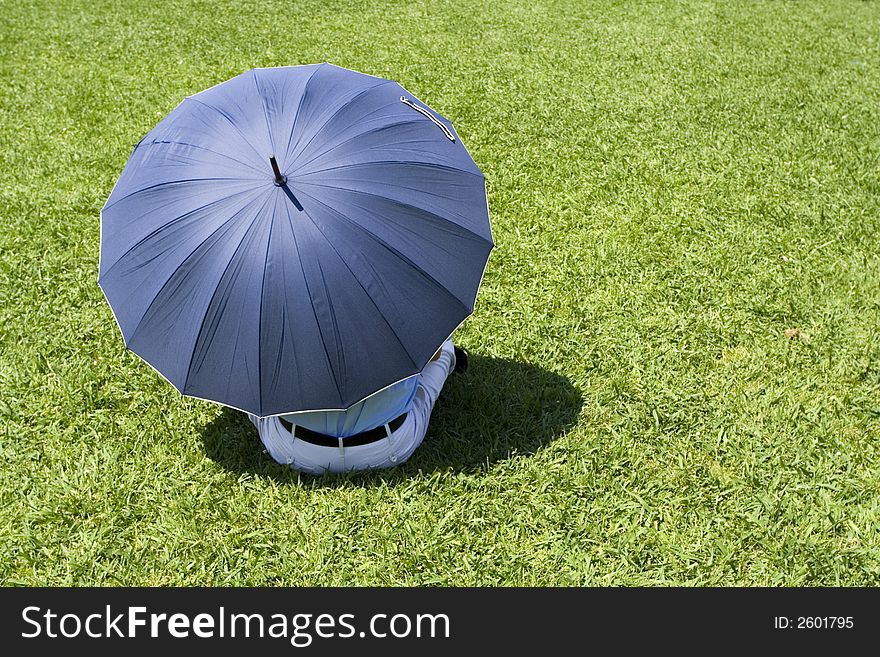 Lonely man sitting in grass with blue umbrella - conceptual