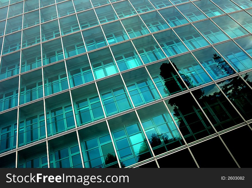 Reflections of trees in the side of a towering, glass-fronted office block