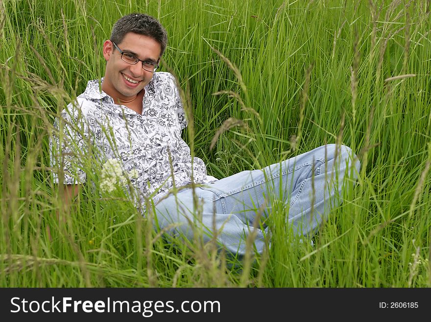 Boy worn eyeglasses sits in high green grass, smiling face. Boy worn eyeglasses sits in high green grass, smiling face