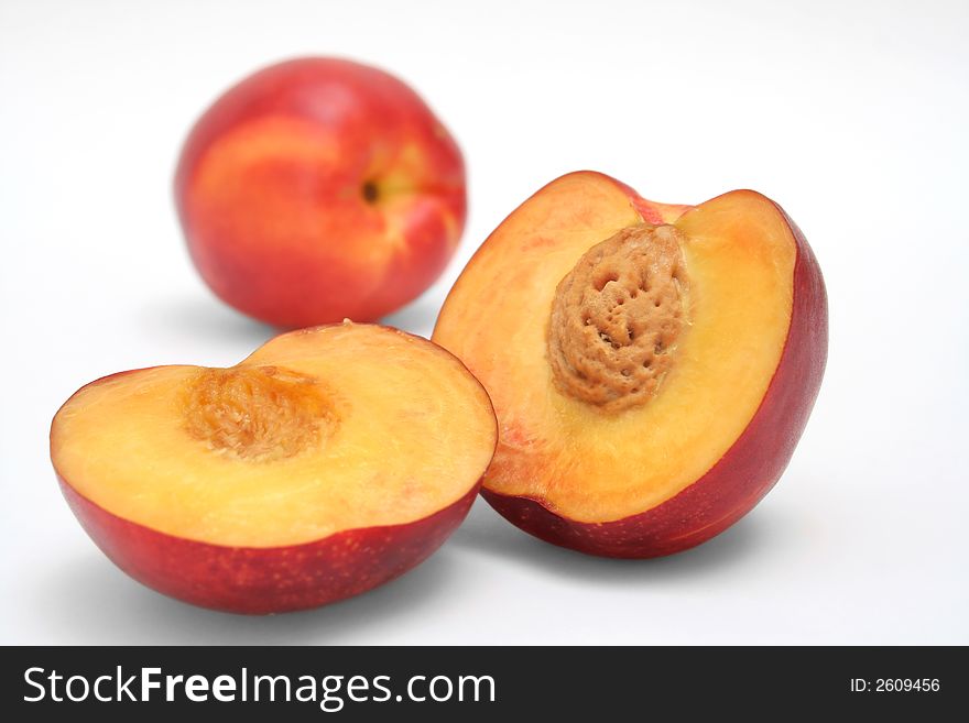 A peach cut in halves with a whole one at the background. A peach cut in halves with a whole one at the background