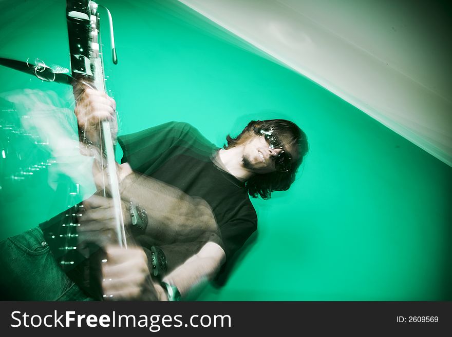 Young man playing electric guitar over green background, zoom and strobe lighting. Young man playing electric guitar over green background, zoom and strobe lighting.