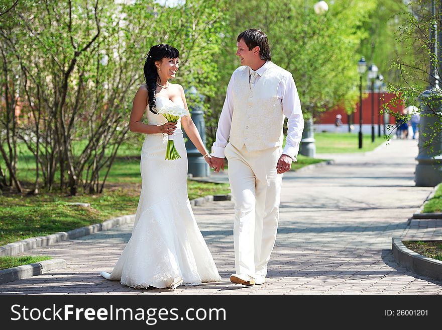 Happy groom and happy bride walking in park