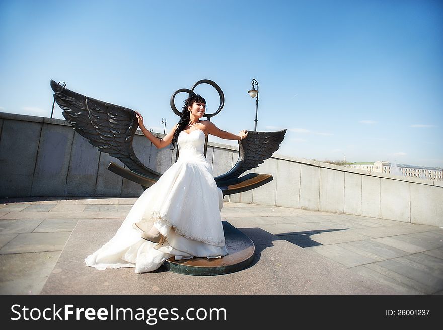 Bride on bronze bench with wings in sunny wedding day