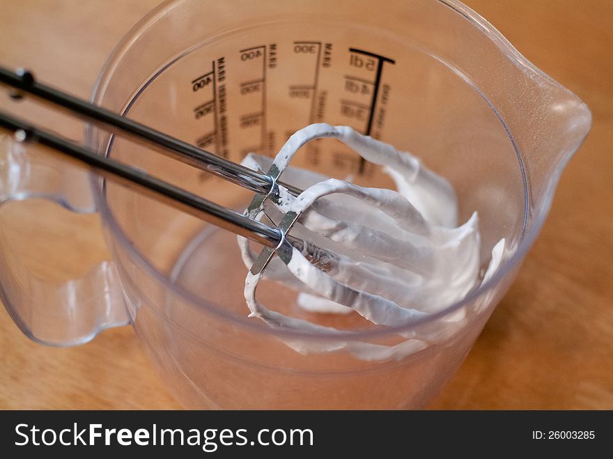 Two electric mixer blades covered in meringue in a measuring cup. Two electric mixer blades covered in meringue in a measuring cup.