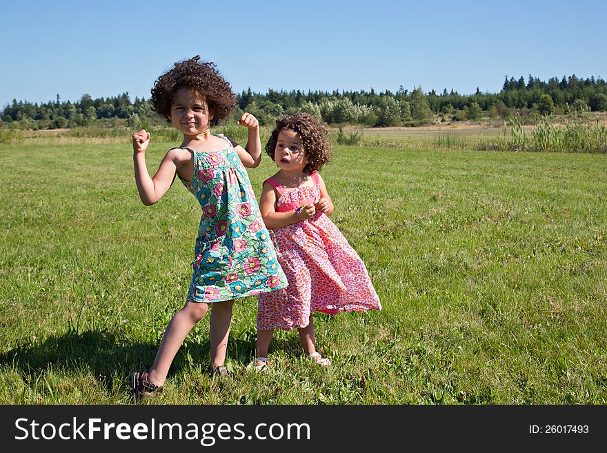 Young healthy preschooler standing in grass field with her sister making muscle arms and being strong. Young healthy preschooler standing in grass field with her sister making muscle arms and being strong
