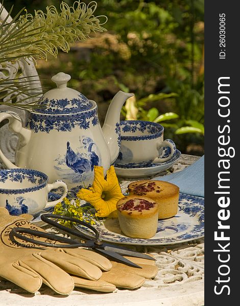 Table set in a garden for tea with cakes, flowers and decorative teapot and cups. Table set in a garden for tea with cakes, flowers and decorative teapot and cups.