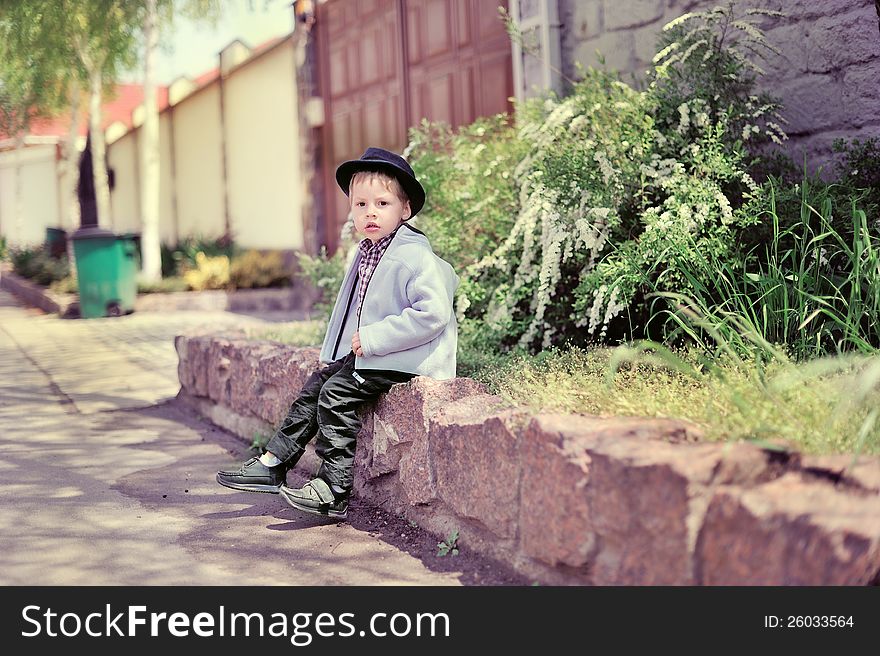 The boy sits on a fence in a blue cap. The boy sits on a fence in a blue cap