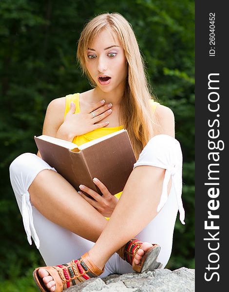 Young woman sitting on a stone,reading a book